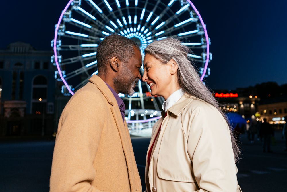 Casal sorridente celebrando o Dia dos Namorados em frente à roda gigante iluminada, mostrando conexão e alegria.