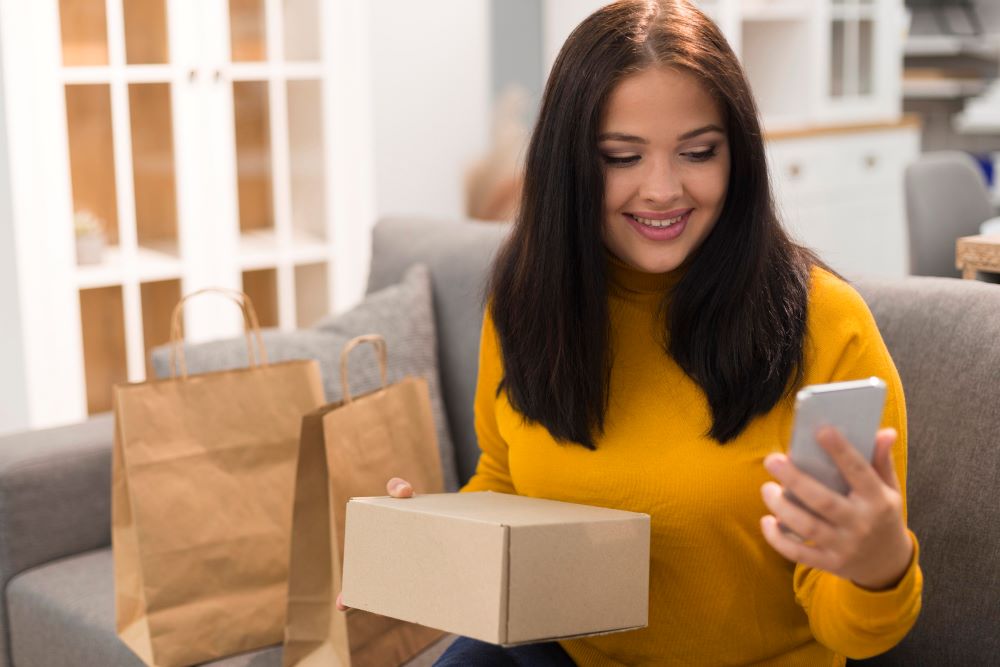 Mulher sorridente segurando um pacote enquanto usa o smartphone, representando compras online e campanhas de remarketing no pós-Black Friday.