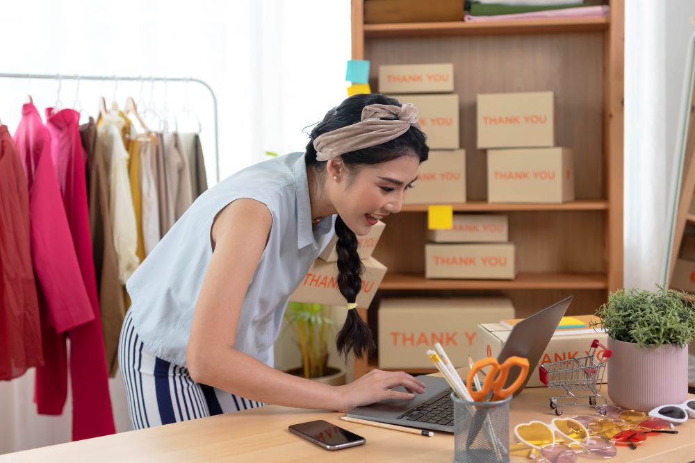 Empreendedora gerenciando a gestão financeira de seu e-commerce em um espaço organizado com produtos e embalagens prontas para envio.