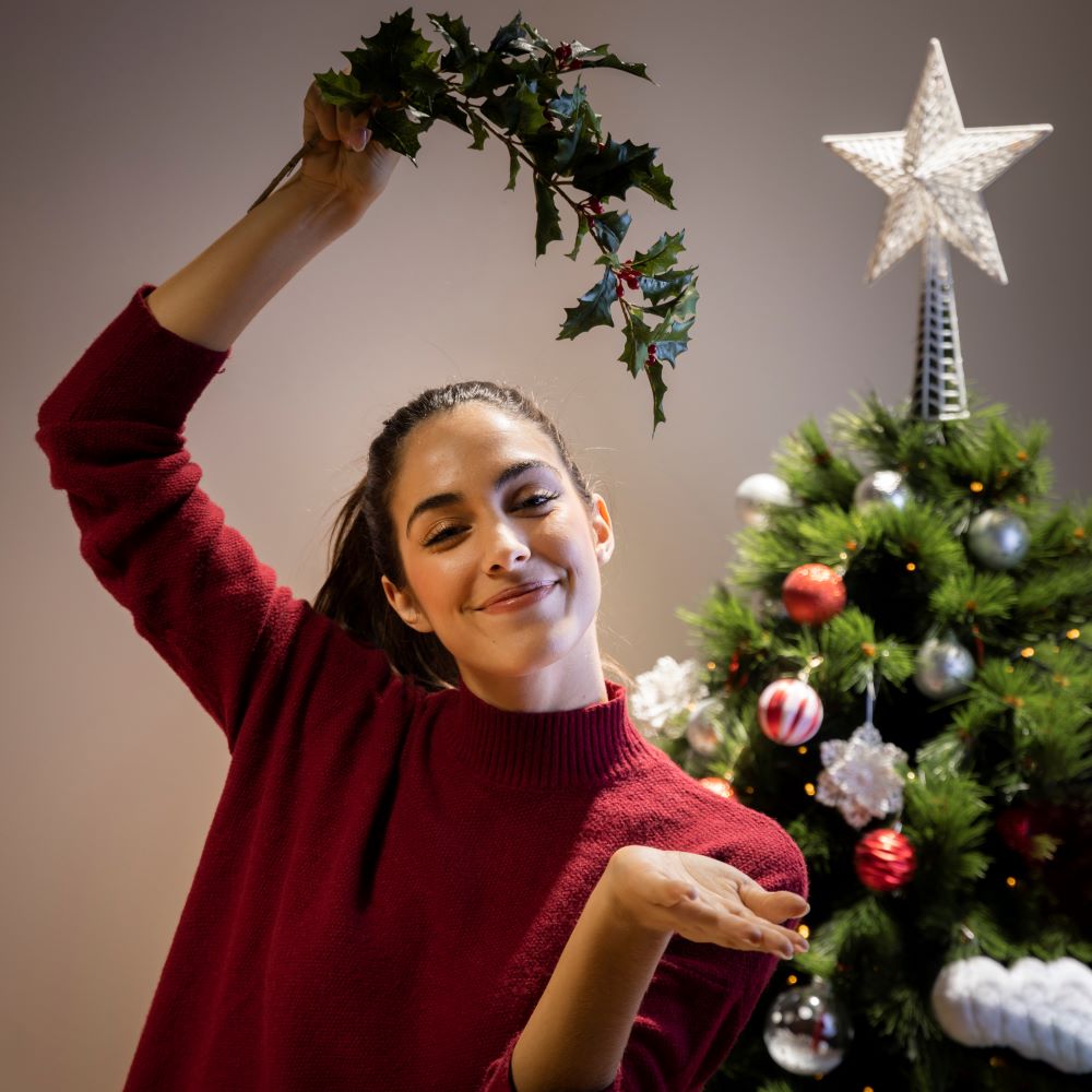 Mulher sorrindo ao lado de uma árvore de Natal decorada, simbolizando o espírito natalino ideal para promoções de Natal em e-commerce