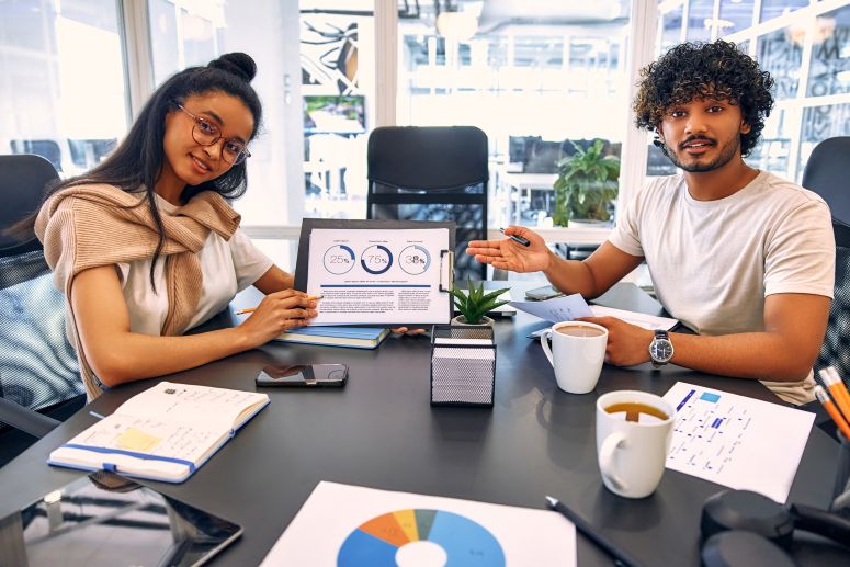 Dois profissionais apresentando gráficos e dados em uma reunião, simbolizando a análise e otimização do ciclo de vendas em um negócio.