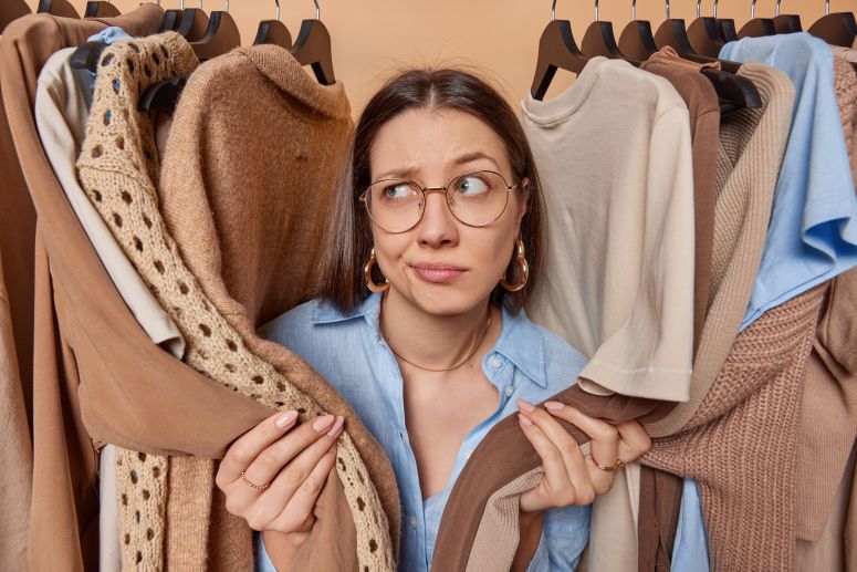 "Mulher indecisa entre várias opções de roupas, representando a escolha entre e-commerce e marketplace para vender produtos.