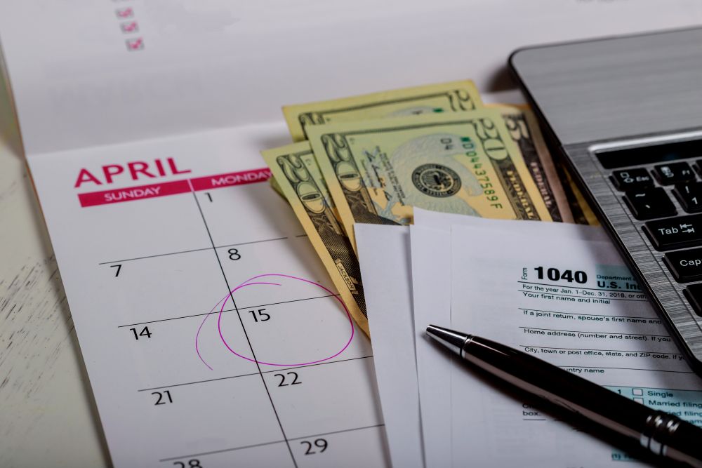 "Calendário de abril, dinheiro e documentos financeiros ao lado de um laptop, representando a importância de monitorar o MRR (Receita Recorrente Mensal) para gestão financeira e previsibilidade nos negócios