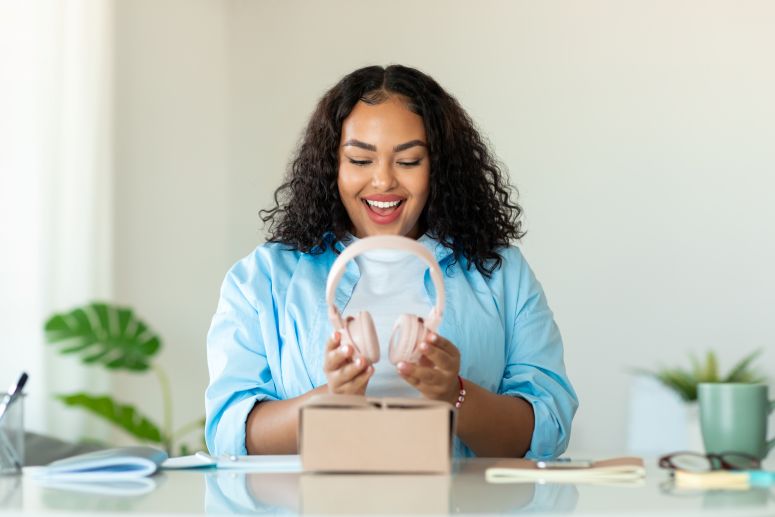 Mulher sorrindo ao abrir uma caixa e visualizar fones de ouvido, simbolizando a popularidade e o apelo de um produto estrela que atrai consumidores.