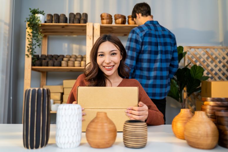 Mulher sorrindo enquanto prepara pacotes para envio, simbolizando o trabalho de um seller que utiliza marketplaces para vender seus produtos.