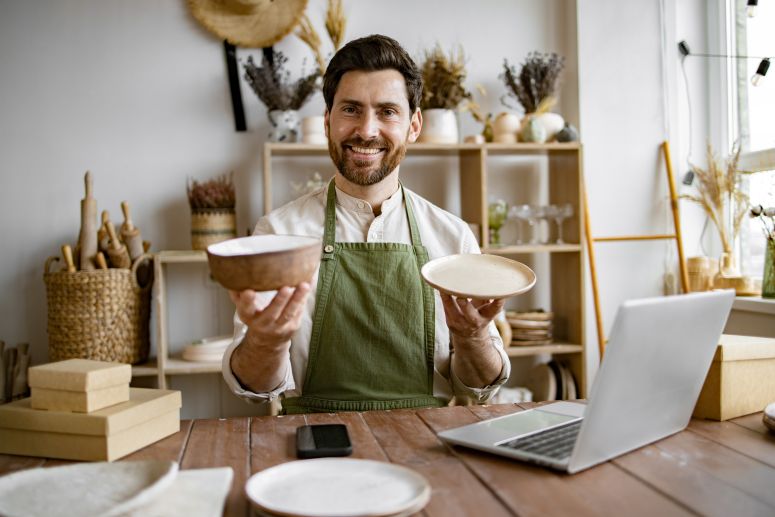 Empreendedor analisando mix de produtos artesanais para vender online, com pratos e tigelas em ambiente decorado