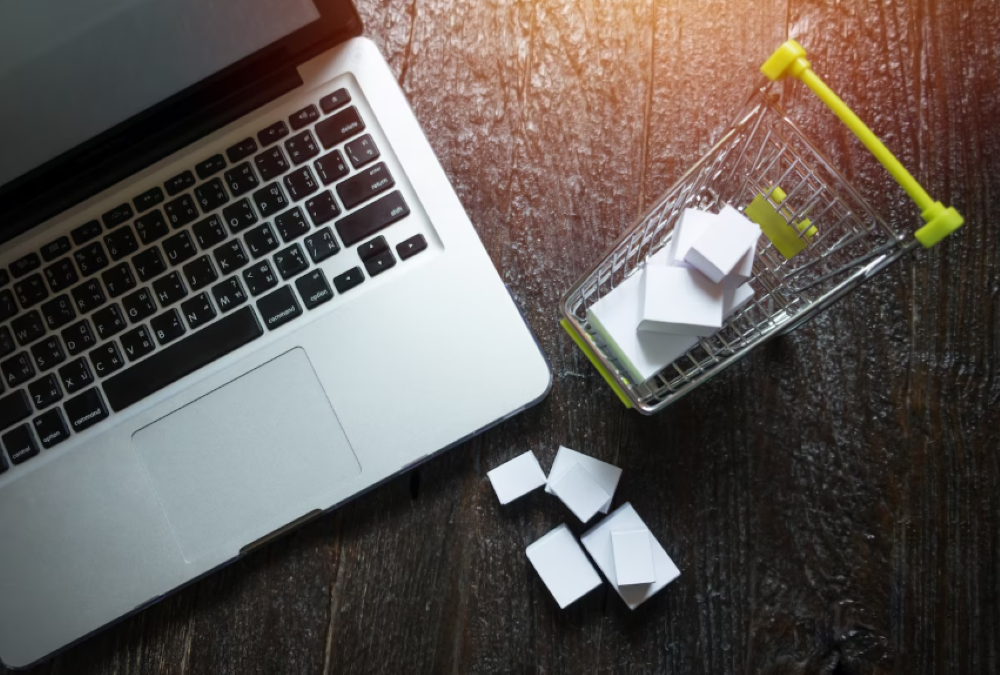 Carrinho de compras em miniatura com pequenas caixas ao lado de um notebook sobre uma mesa de madeira, representando o abandono de carrinho no e-commerce.