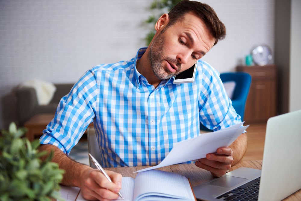 Homem multitarefas analisando documentos e falando ao telefone, representando a gestão de XML da nota fiscal em loja virtual