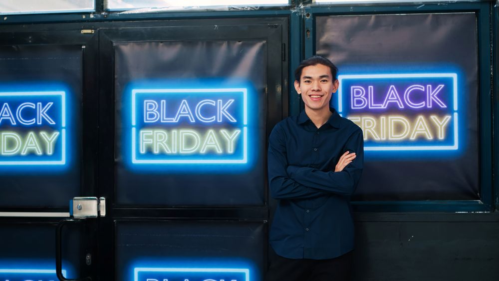 Empreendedor sorrindo em frente a painéis de Black Friday, representando lojista que aprendeu como calcular lucro em promoções