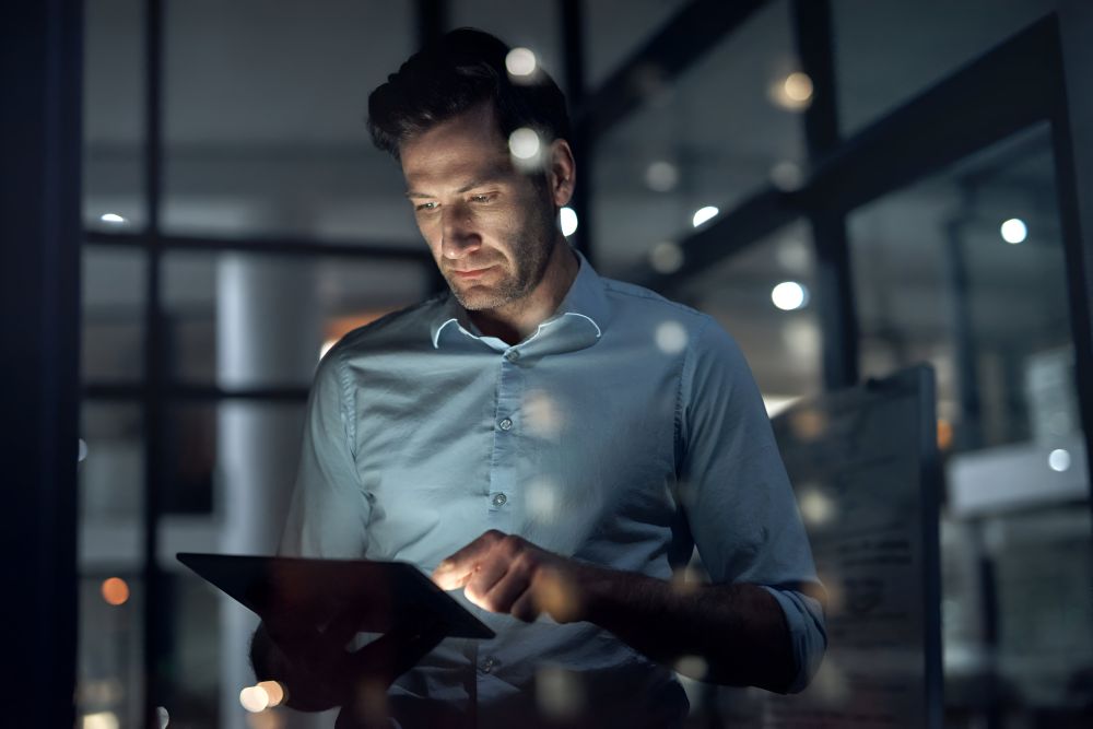 Homem usando tablet à noite em escritório, representando o uso de ERP na prática para gestão eficiente de pedidos e estoque no e-commerce