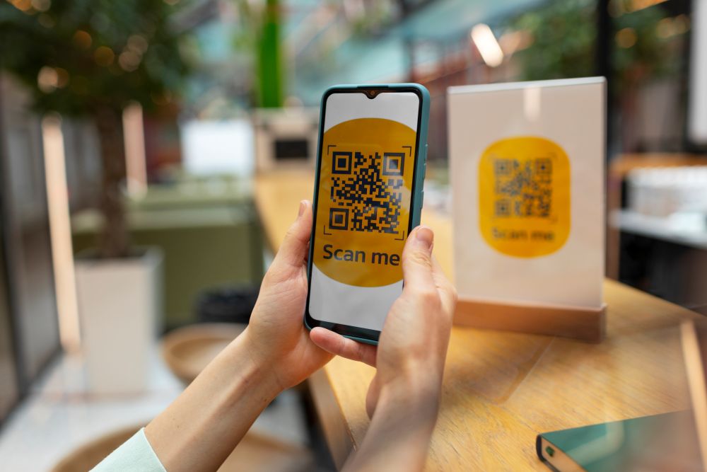 Pessoa segurando um smartphone e escaneando um QR Code em um restaurante, representando o uso prático da ferramenta gratuita Bagy QR Code Generator