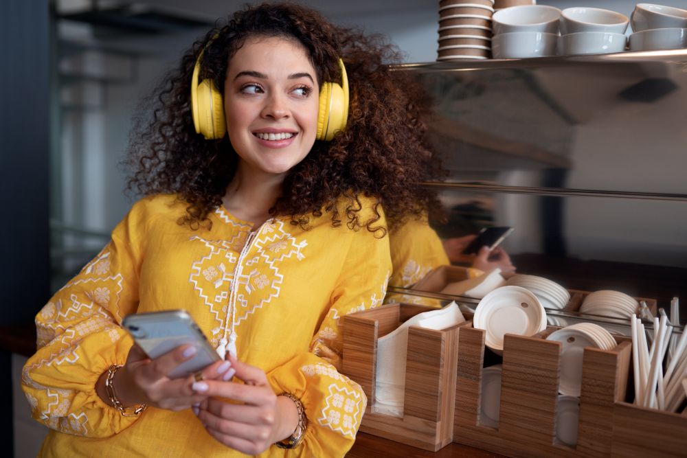 Mulher sorridente com fones de ouvido amarelos e celular nas mãos, representando criatividade e inspiração para escolher frases para bio do Instagram.