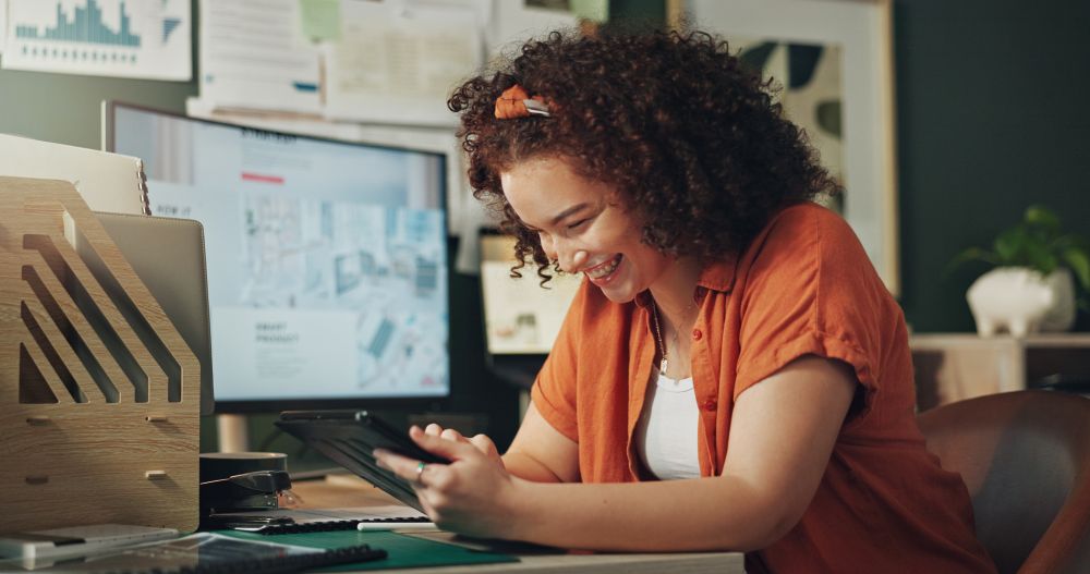 Empreendedora sorrindo enquanto usa tablet em escritório criativo, representando sucesso com collabs no Instagram.