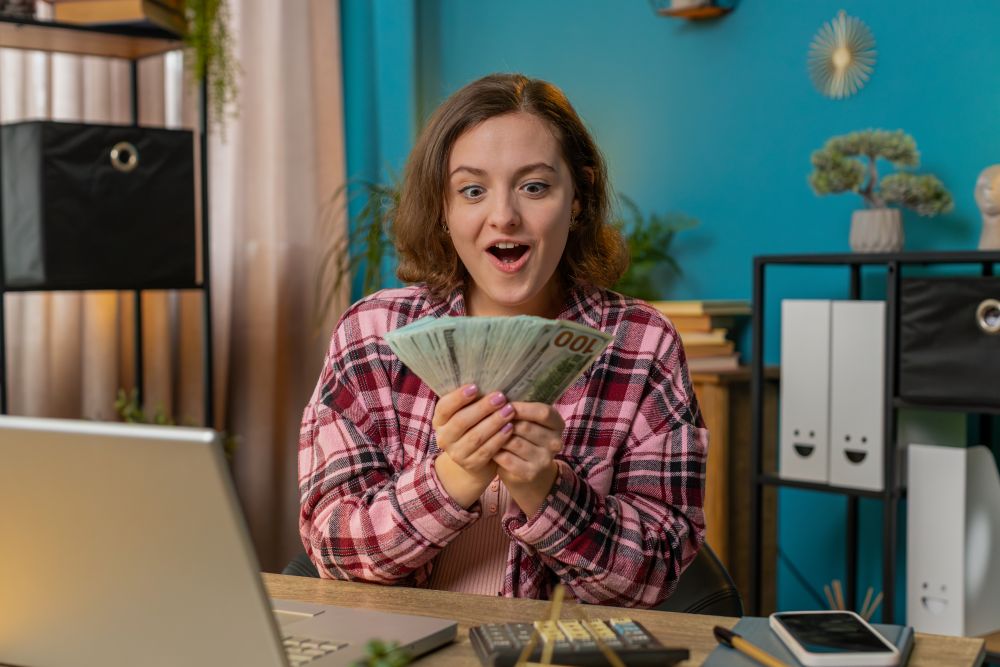 Empreendedora em home office comemorando ganhos financeiros com renda extra online usando o computador.